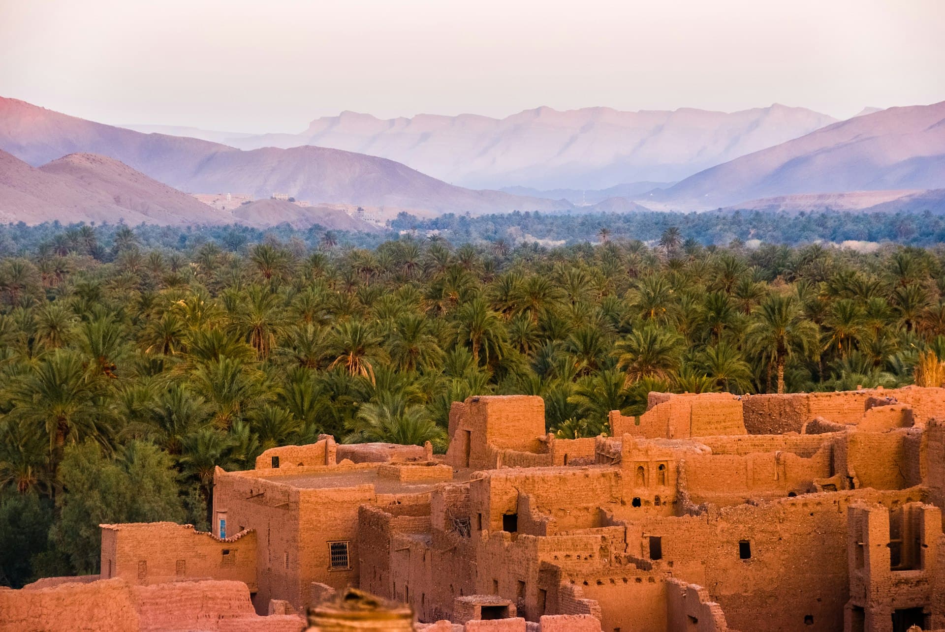 Tourist riding a quad bike through golden Agadir sand dunes at sunset with Atlas Mountains in the background